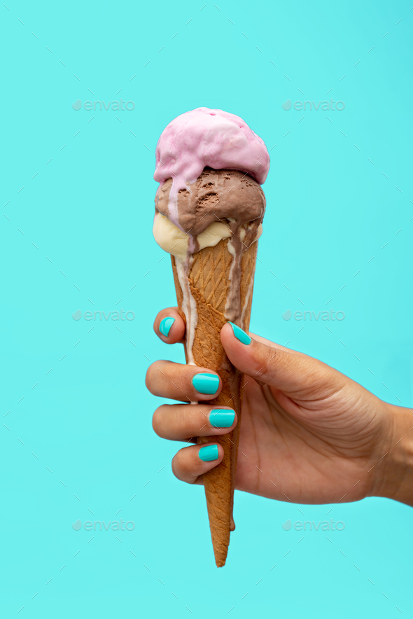Woman's hand holding an ice cream cone melting over a light blue
